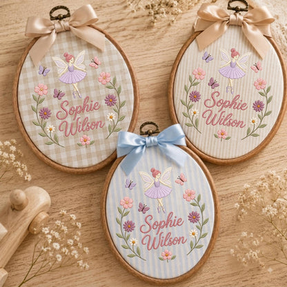 May include: Three oval wooden embroidery hoops featuring fabric backgrounds with gingham, pinstripe, and vertical stripe patterns. Each hoop displays an embroidered fairy, floral wreath, butterflies, and the name Sophie Wilson in pink script.