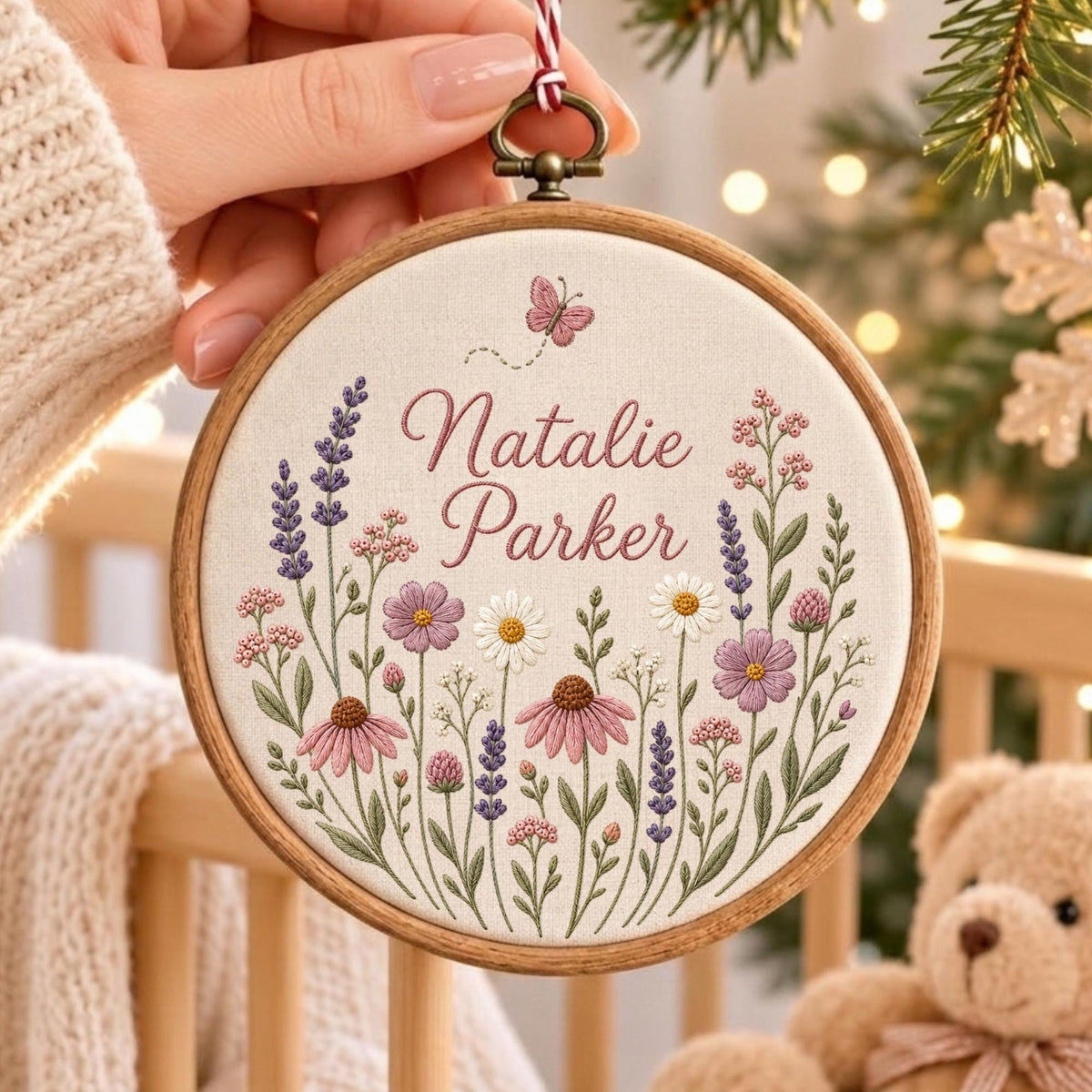 May include: A circular wooden embroidery hoop containing off-white fabric with hand-stitched floral designs in shades of pink, purple, and green. The text Natalie Parker is embroidered in dark pink script, accompanied by a small butterfly above.