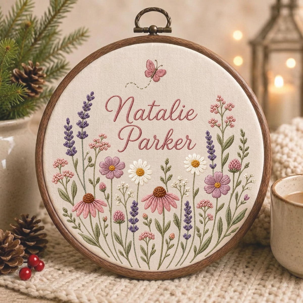 May include: A circular wooden embroidery hoop containing cream fabric with hand-stitched floral designs in shades of pink, purple, and white. The text "Natalie Parker" is embroidered in dark pink script, accompanied by a small pink butterfly above.