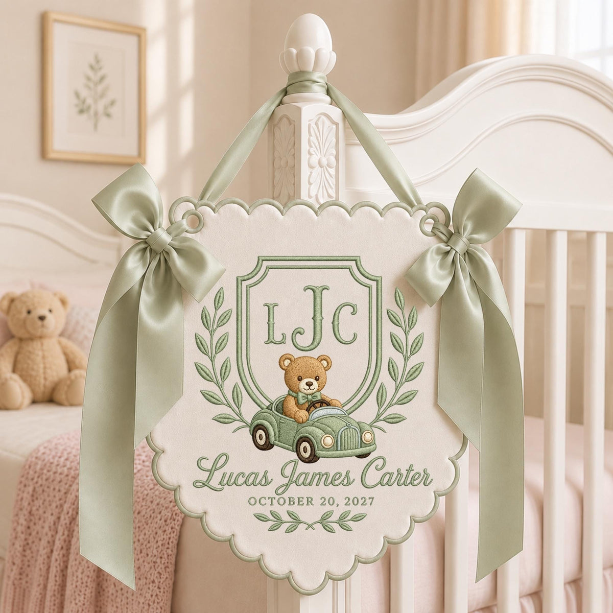 May include: A cream-colored scalloped wall hanging featuring sage green embroidery of a teddy bear driving a vintage car, the initials LJC, the name Lucas James Carter, and the date OCTOBER 20, 2027, accented with two sage green satin ribbon bows.