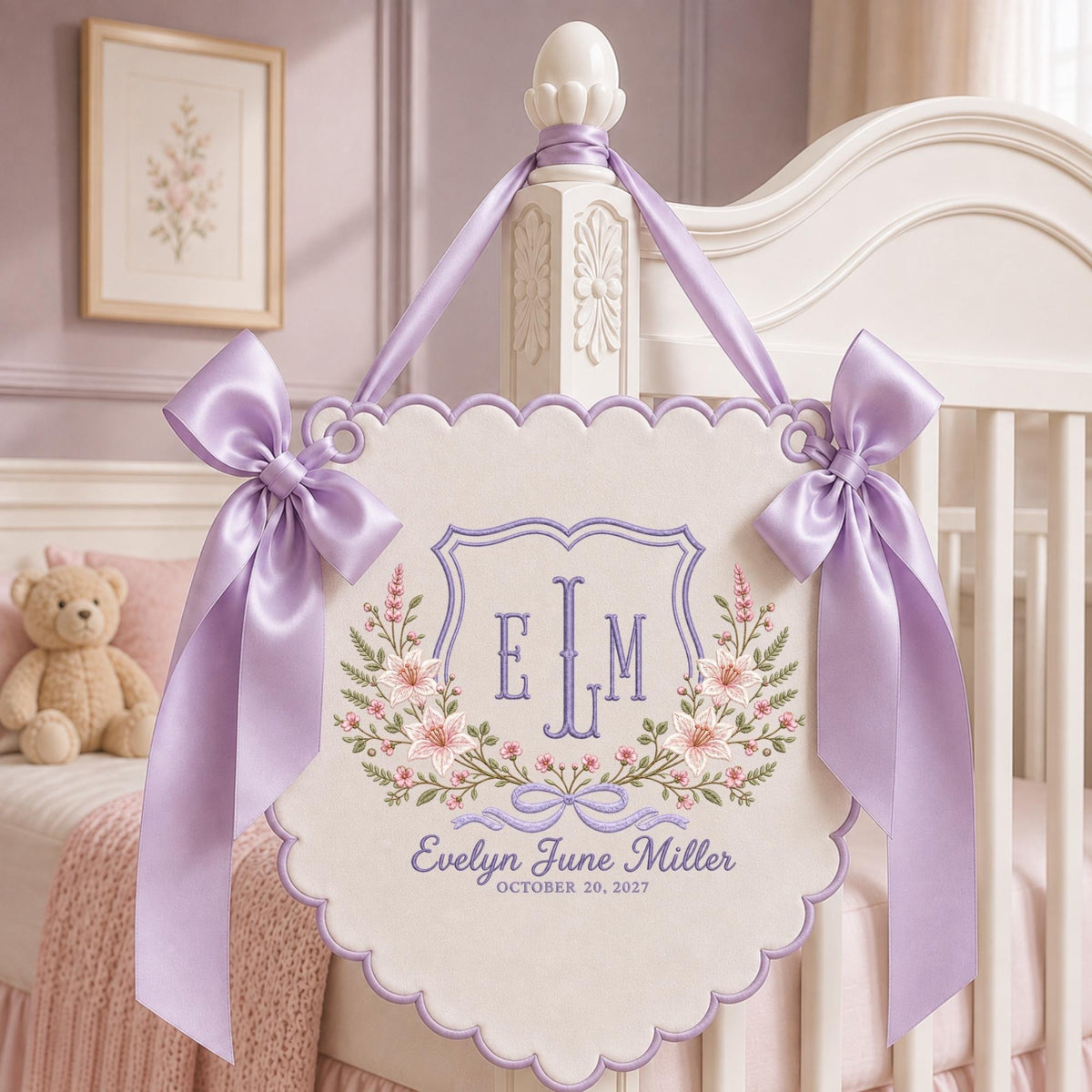 May include: A cream-colored fabric wall hanging with scalloped edges, featuring purple embroidered floral motifs, a central shield with the monogram ELM, and the text Evelyn June Miller October 20, 2027. Two large lavender satin bows adorn the top corners.