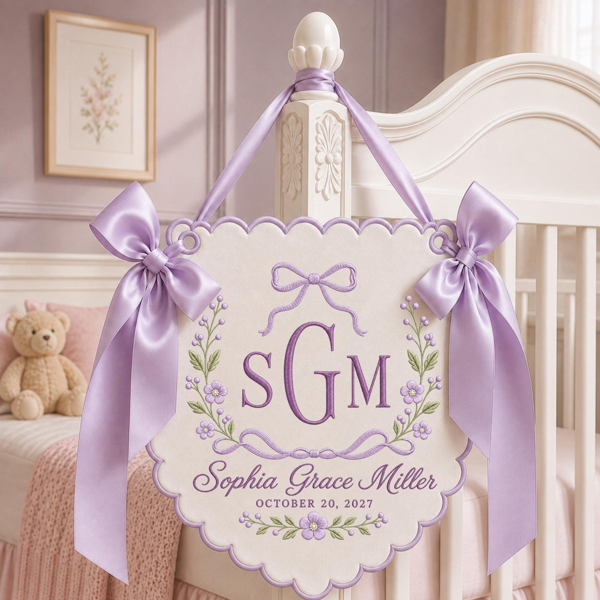 May include: A cream-colored scalloped wall hanging featuring purple embroidery of the monogram SGM, the name Sophia Grace Miller, and the date October 20, 2027. The piece is decorated with floral vines and bows, finished with two large lavender satin ribbons.