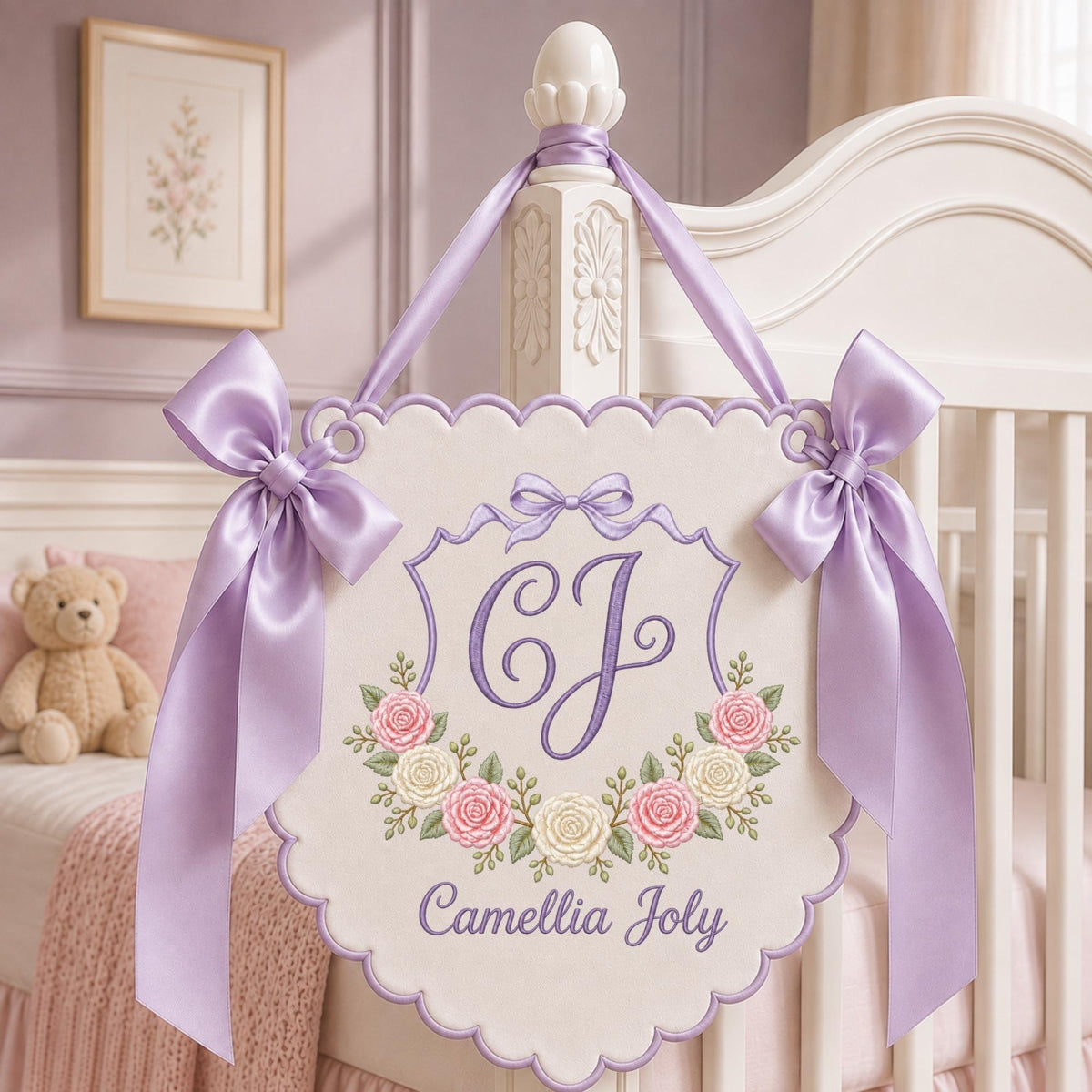 May include: A cream-colored fabric wall hanging with a scalloped edge, featuring an embroidered purple monogram of the letters CJ, a floral wreath of pink and white roses, and the name Camellia Joly in purple script, accented by lavender satin bows.