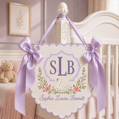 May include: A cream-colored scalloped wall hanging featuring a purple embroidered monogram SLB, a white swan illustration, and floral accents. The sign is suspended by a lavender satin ribbon with large bows on each side and includes the name Sophia Louise Bennett embroidered in purple script at the bottom.