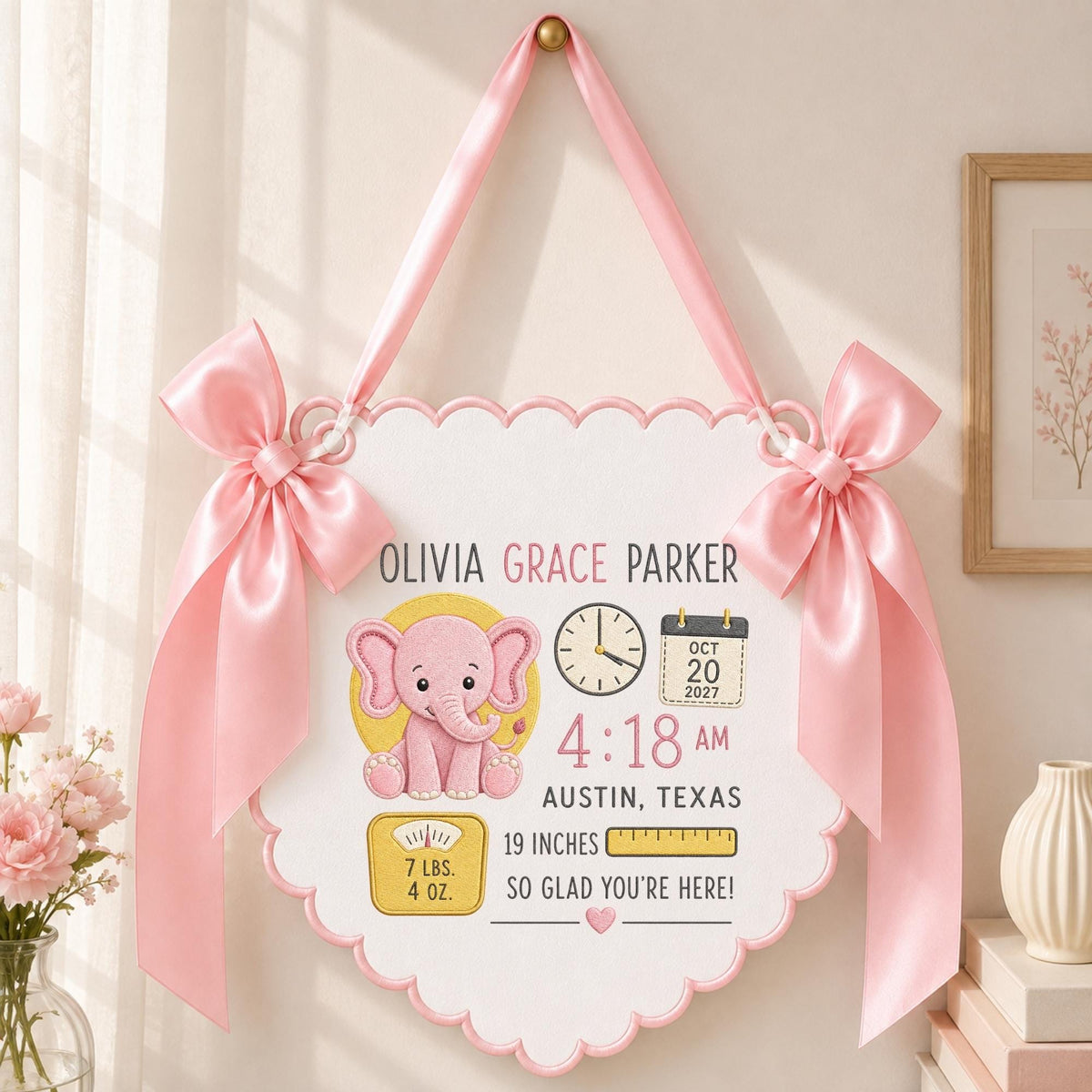 May include: A white scalloped wall hanging featuring a pink elephant illustration, the name Olivia Grace Parker, birth details including 4:18 AM, Oct 20 2027, Austin, Texas, 19 inches, and 7 lbs. 4 oz., accented by two large pink satin bows.