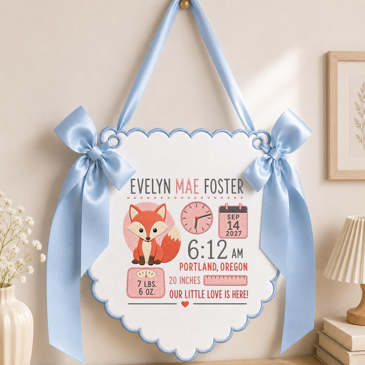 May include: A white scalloped wall hanging with light blue trim and satin bows, featuring a fox illustration and text: EVELYN MAE FOSTER, SEP 14 2027, 6:12 AM, PORTLAND, OREGON, 7 LBS. 6 OZ., 20 INCHES, and OUR LITTLE LOVE IS HERE! with a clock icon.
