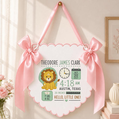 May include: A white scalloped wall hanging featuring a cartoon lion, a clock showing 4:18, a calendar dated Oct 20, 2027, and text reading Theodore James Clark, Austin, Texas, 20 inches, 7 lbs. 4 oz., and Hello, Little One, with pink satin bows.