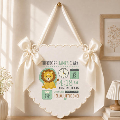 May include: A cream-colored scalloped wall hanging featuring a lion illustration, a clock, a calendar showing Oct 20 2027, and text including Theodore James Clark, 4:18 AM, Austin, Texas, 20 inches, 7 lbs. 4 oz., and Hello, Little One! with satin bows.
