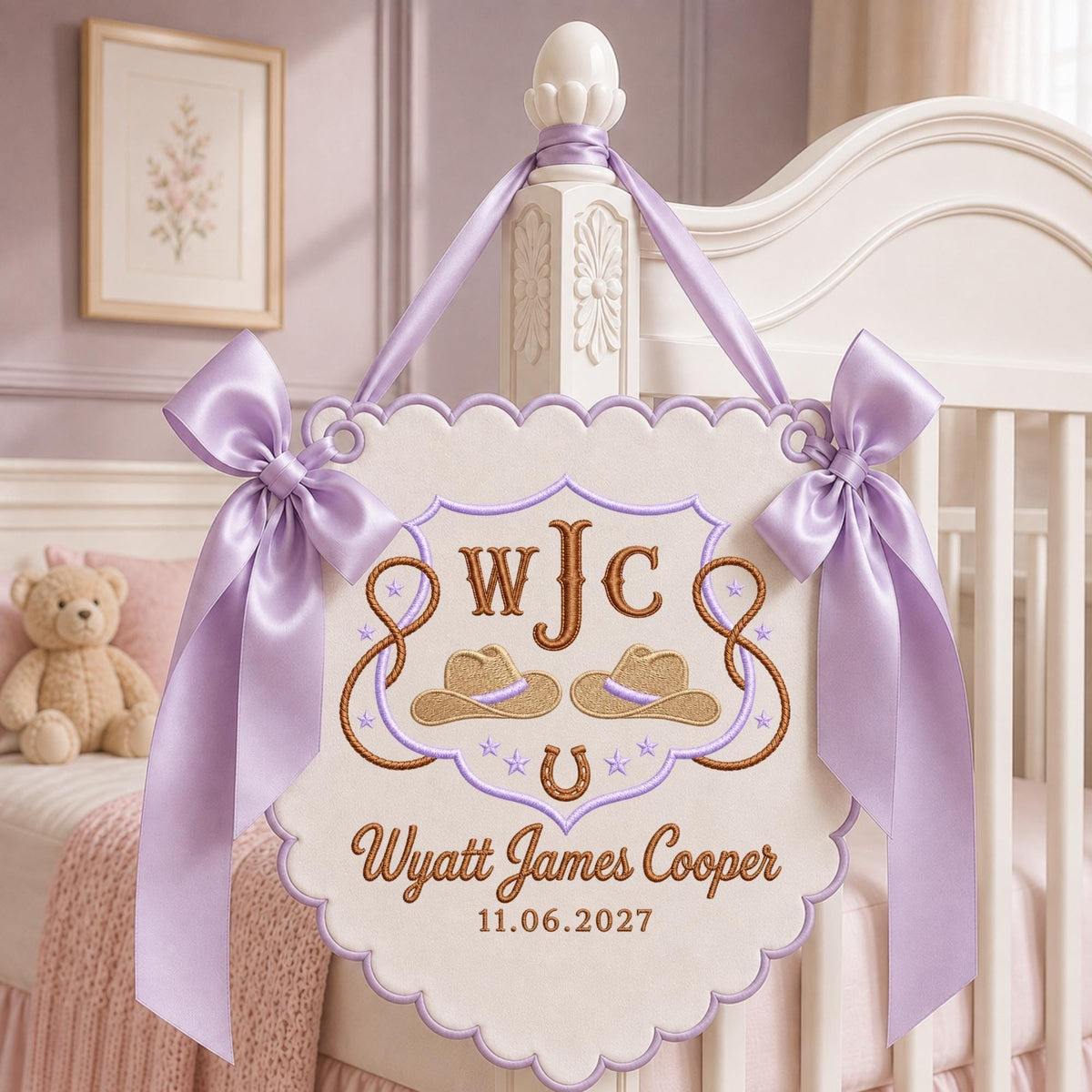 May include: A cream-colored scalloped wall hanging featuring lavender satin bows and embroidery. The design includes the monogram WJC, two cowboy hats, a horseshoe, and the text Wyatt James Cooper with the date 11.06.2027 in brown thread.