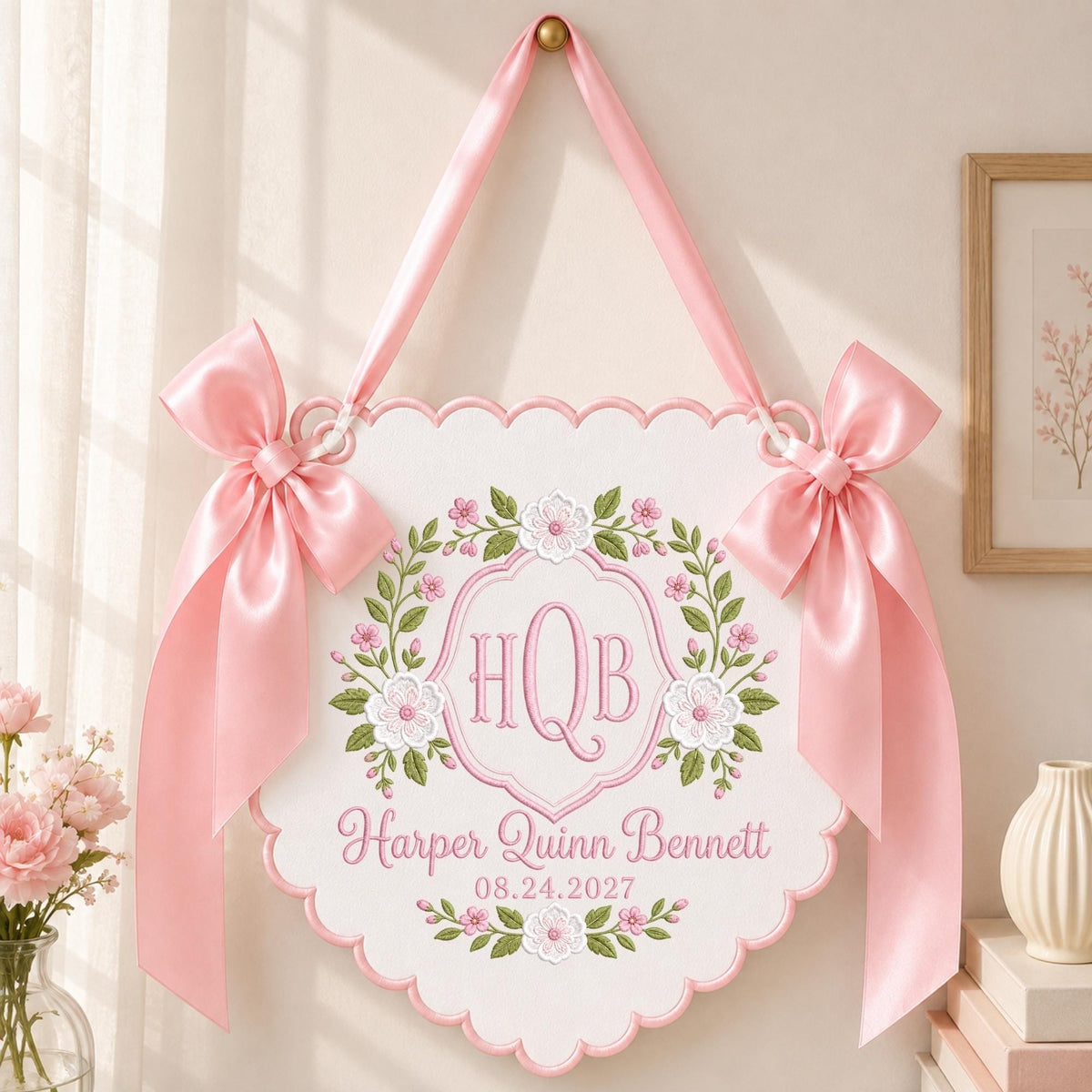 May include: A white scalloped wall hanging featuring pink satin bows on each side. The center displays embroidered pink floral wreaths surrounding the monogram HQB, the name Harper Quinn Bennett, and the date 08.24.2027 in pink script lettering.