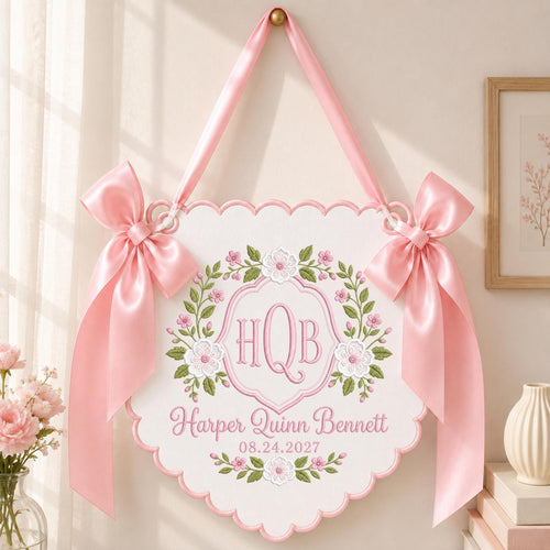 May include: A white scalloped wall hanging featuring pink satin bows on each side. The center displays embroidered pink floral wreaths surrounding the monogram HQB, the name Harper Quinn Bennett, and the date 08.24.2027 in pink script lettering.