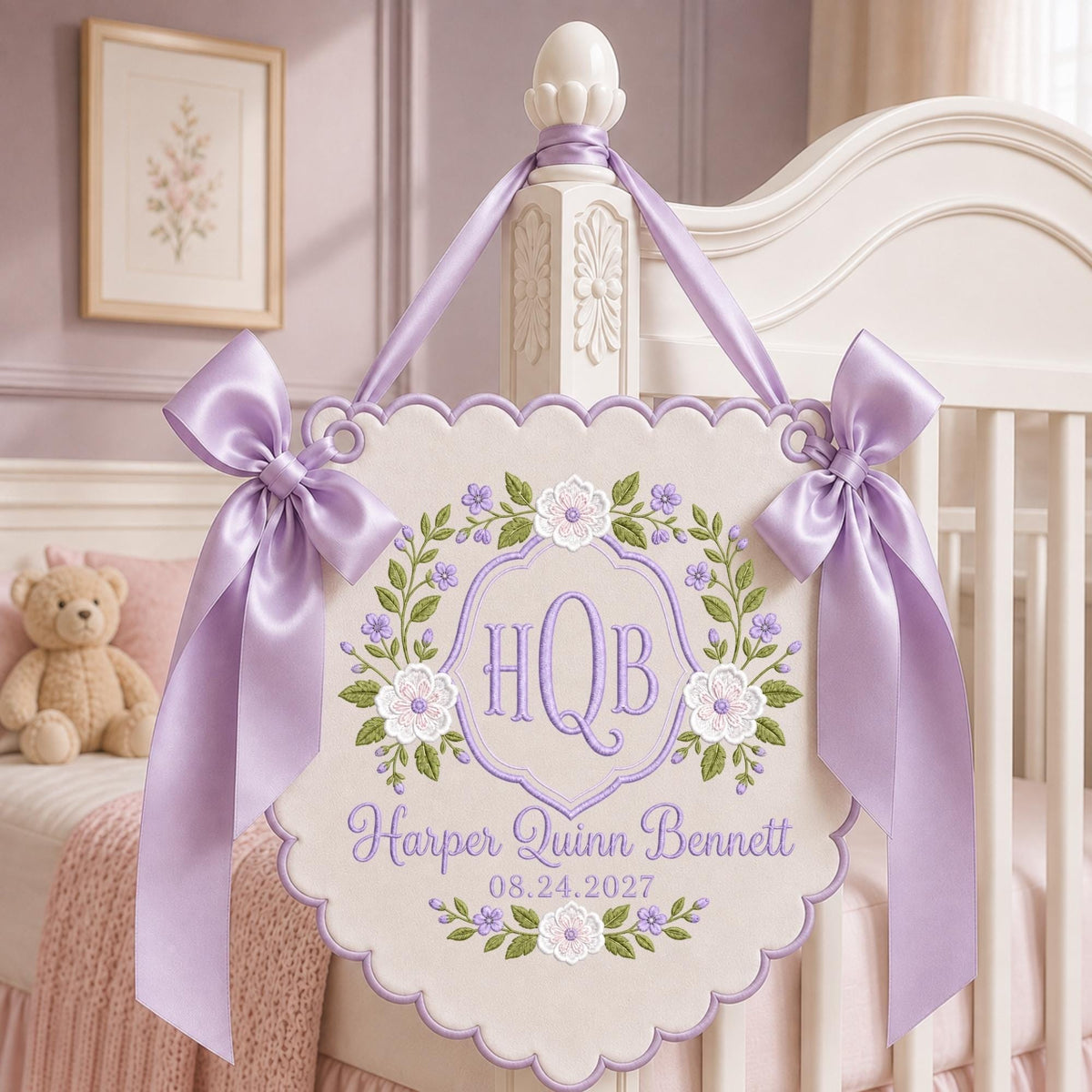 May include: A scalloped, cream-colored fabric wall hanging featuring lavender embroidery of a floral wreath, the monogram "HQB," the name "Harper Quinn Bennett," and the date "08.24.2027." It is adorned with two large, shiny lavender satin bows.
