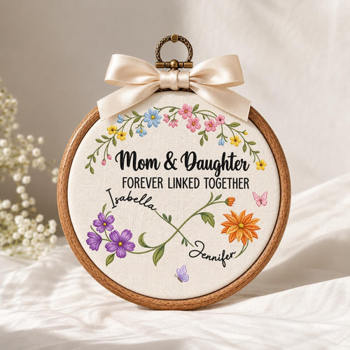 May include: A circular wooden embroidery hoop containing white fabric with the text Mom &amp; Daughter FOREVER LINKED TOGETHER. The design features a floral infinity symbol with the names Isabella and Jennifer, accented by colorful flowers and butterflies.