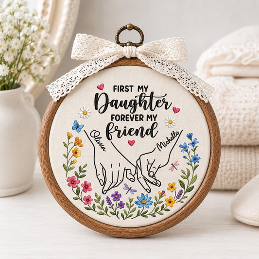 May include: A circular wooden embroidery hoop containing white fabric with the text FIRST MY Daughter FOREVER MY friend. The design features two hands pinky promising, the names Olivia and Michelle, and a colorful floral border with small hearts.