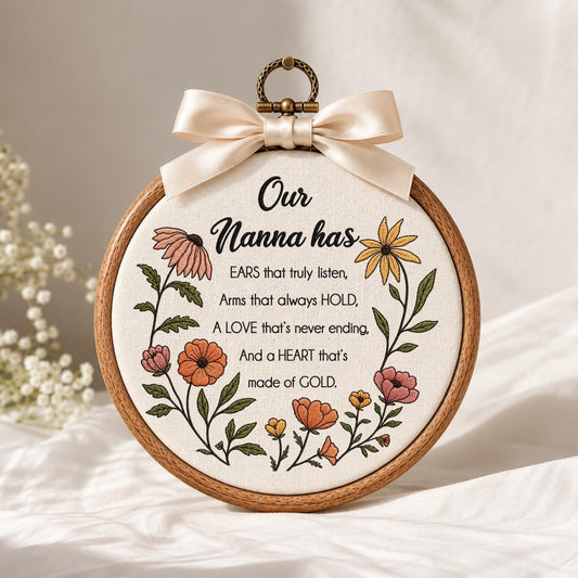 May include: A circular wooden embroidery hoop containing cream-colored fabric with floral embroidery and the text: Our Nanna has EARS that truly listen, Arms that always HOLD, A LOVE that's never ending, And a HEART that's made of GOLD. A cream satin bow is attached to the top.