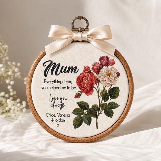 May include: A circular wooden embroidery hoop containing cream fabric with a floral design of red and white roses. The text reads: Mum, Everything I am, you helped me to be. Love you always, Chloe, Vanessa &amp; Jordan x. A cream satin bow sits at the top.