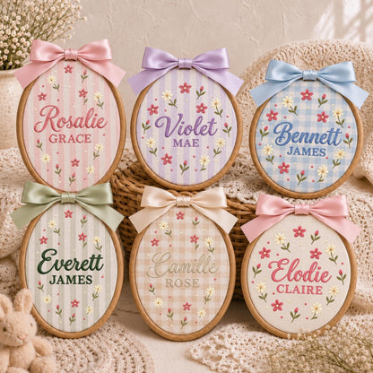 May include: Six oval wooden embroidery hoops featuring personalized names and middle names stitched in various colors. Each hoop is decorated with embroidered floral patterns and topped with a satin ribbon bow in coordinating pastel colors.