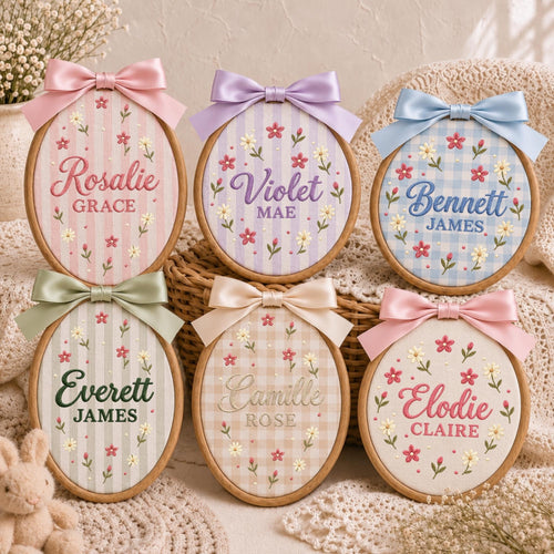 May include: Six oval wooden embroidery hoops featuring personalized names and middle names stitched in various colors. Each hoop is decorated with embroidered floral patterns and topped with a satin ribbon bow in coordinating pastel colors.