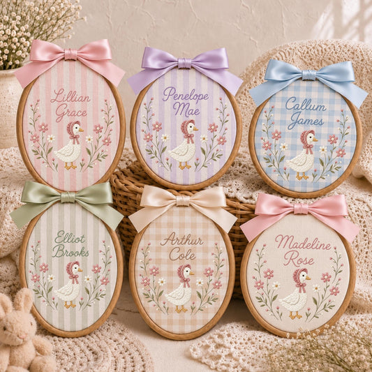 May include: Six oval wooden embroidery hoops featuring fabric backgrounds with various patterns and colors. Each hoop displays a personalized name, a central embroidered duckling wearing a bonnet, and floral accents, topped with a satin bow.
