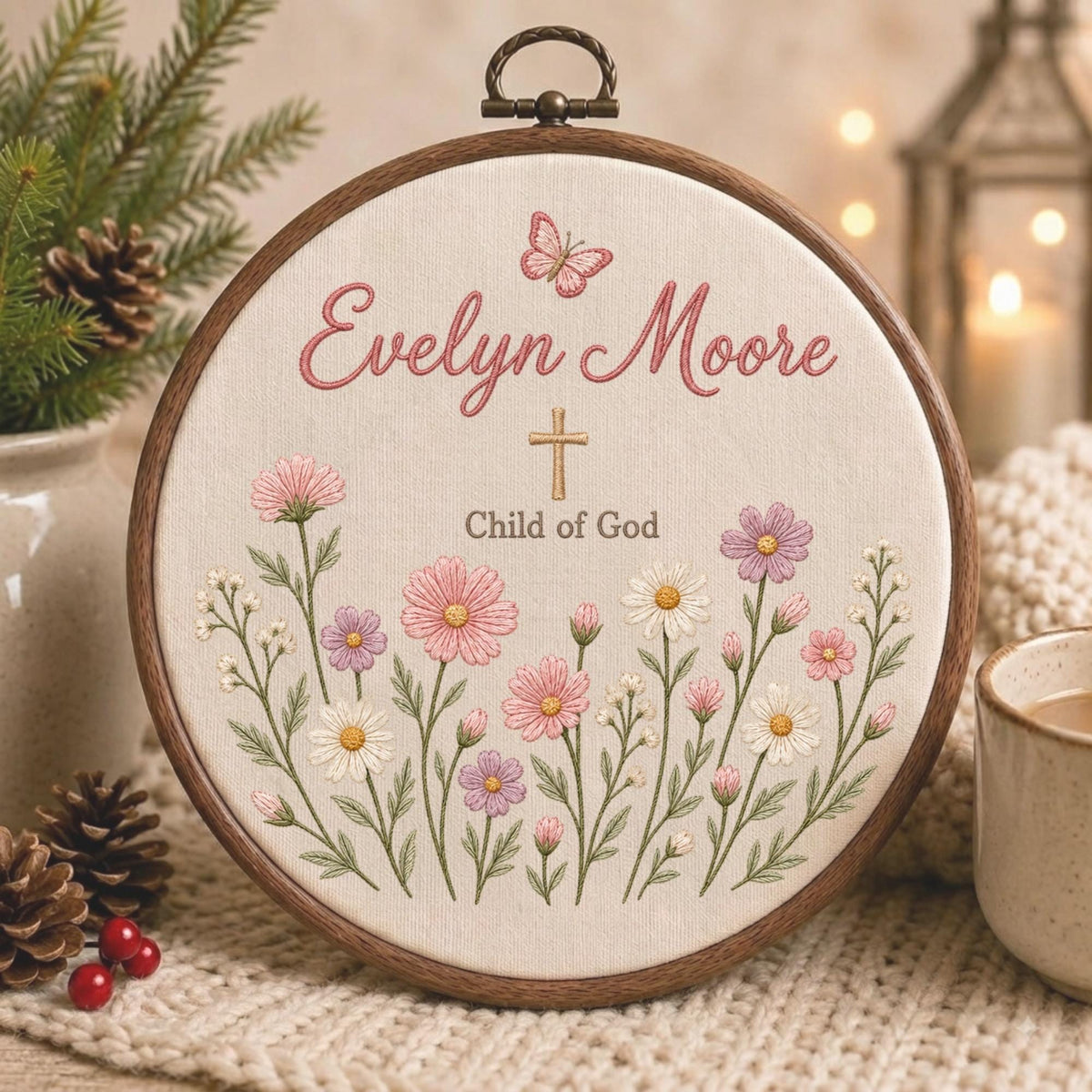 May include: A circular wooden embroidery hoop containing cream-colored fabric with hand-stitched floral designs in pink, purple, and white. The text reads Evelyn Moore and Child of God in brown, with a small pink butterfly and a gold cross above.