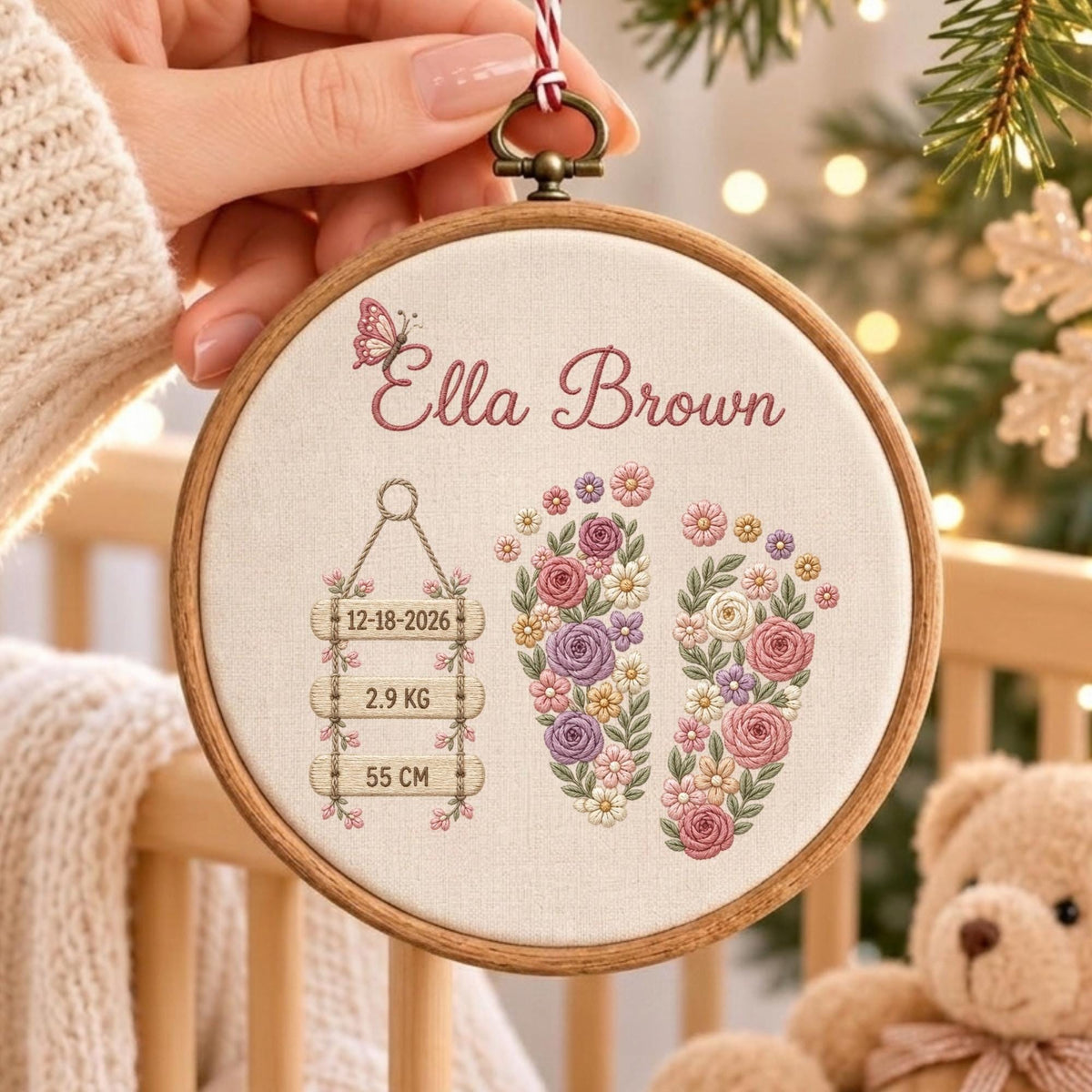 May include: A round wooden embroidery hoop containing cream fabric with the embroidered name Ella Brown, a butterfly, and two floral footprints. A hanging sign displays the date 12-18-2026, the weight 2.9 KG, and the length 55 CM.