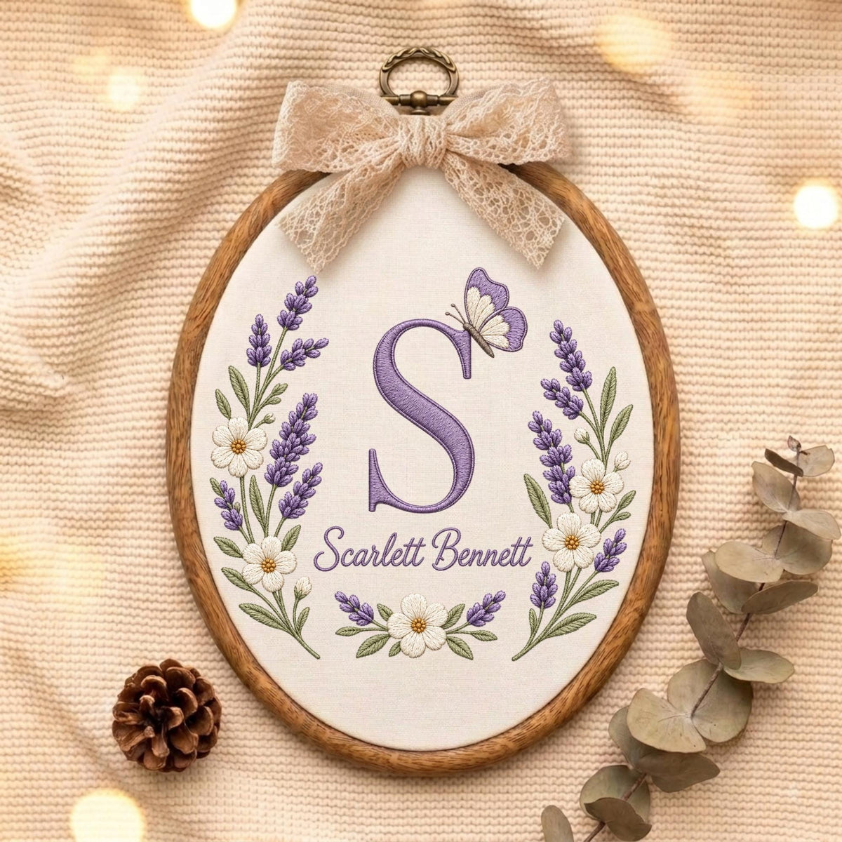 May include: An oval embroidery hoop containing white fabric with a purple embroidered letter S, a butterfly, and lavender floral sprigs. The text Scarlett Bennett is stitched below the letter. A beige lace bow is attached to the top metal hanger.