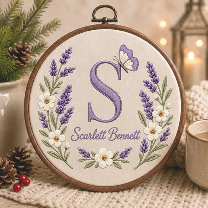 May include: A circular wooden embroidery hoop containing cream-colored fabric with a hand-stitched design. The design features a large purple letter S, a small purple and white butterfly, lavender sprigs, white flowers, and the name Scarlett Bennett.