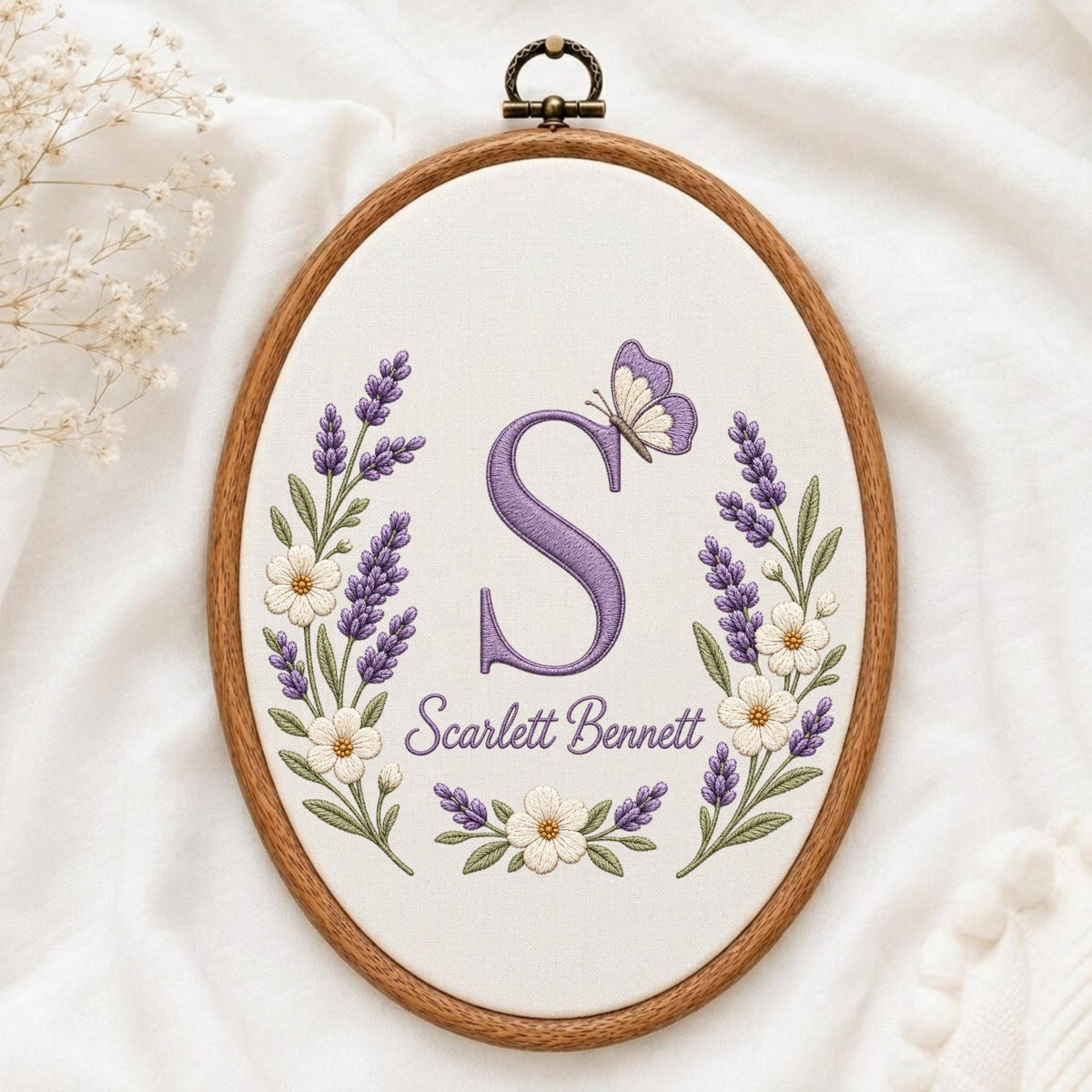 May include: An oval wooden embroidery hoop containing white fabric with a purple embroidered letter S, a purple butterfly, and floral sprigs of lavender and white flowers. The text Scarlett Bennett is embroidered in purple below the letter S.