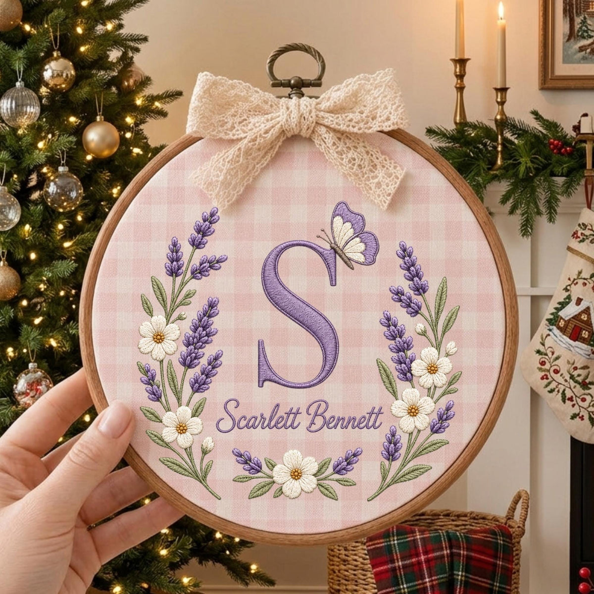 May include: A circular wooden embroidery hoop containing pink and white gingham fabric. The fabric features a large purple letter S, the name Scarlett Bennett, lavender sprigs, white flowers, and a butterfly, topped with a beige lace bow.