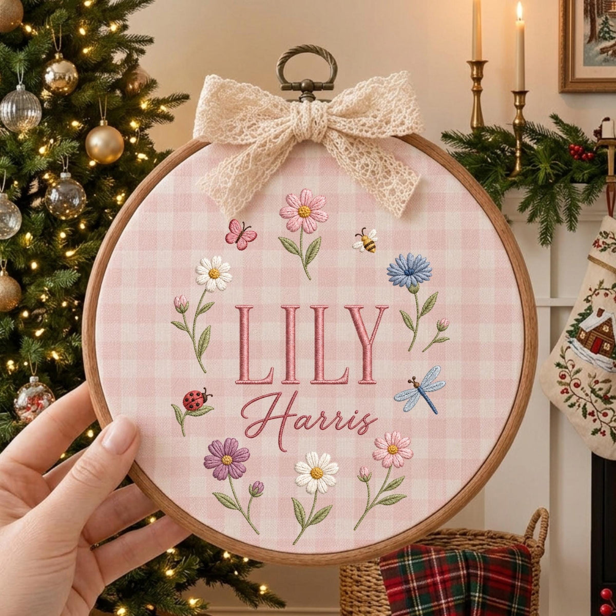 May include: A circular wooden embroidery hoop featuring a light pink and white gingham fabric background. The center is embroidered with the name Lily Harris in pink thread, surrounded by colorful flowers, a ladybug, a bee, and a dragonfly.