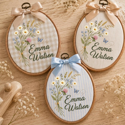 May include: Three oval wooden embroidery hoops featuring fabric backgrounds with gingham, vertical stripes, and light blue stripes. Each hoop displays embroidered wildflowers, a small blue butterfly, and the name Emma Watson in dark green script.