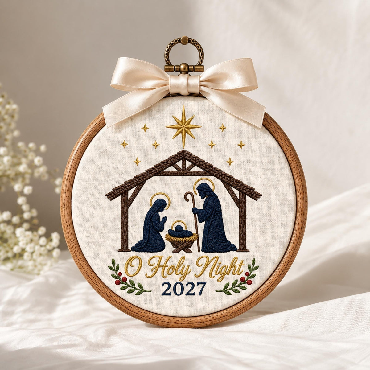 May include: A circular wooden embroidery hoop containing white fabric with a nativity scene featuring Mary, Joseph, and the infant Jesus in a manger. Above is a gold star and small stars. Below is the text O Holy Night 2027 with holly leaves.