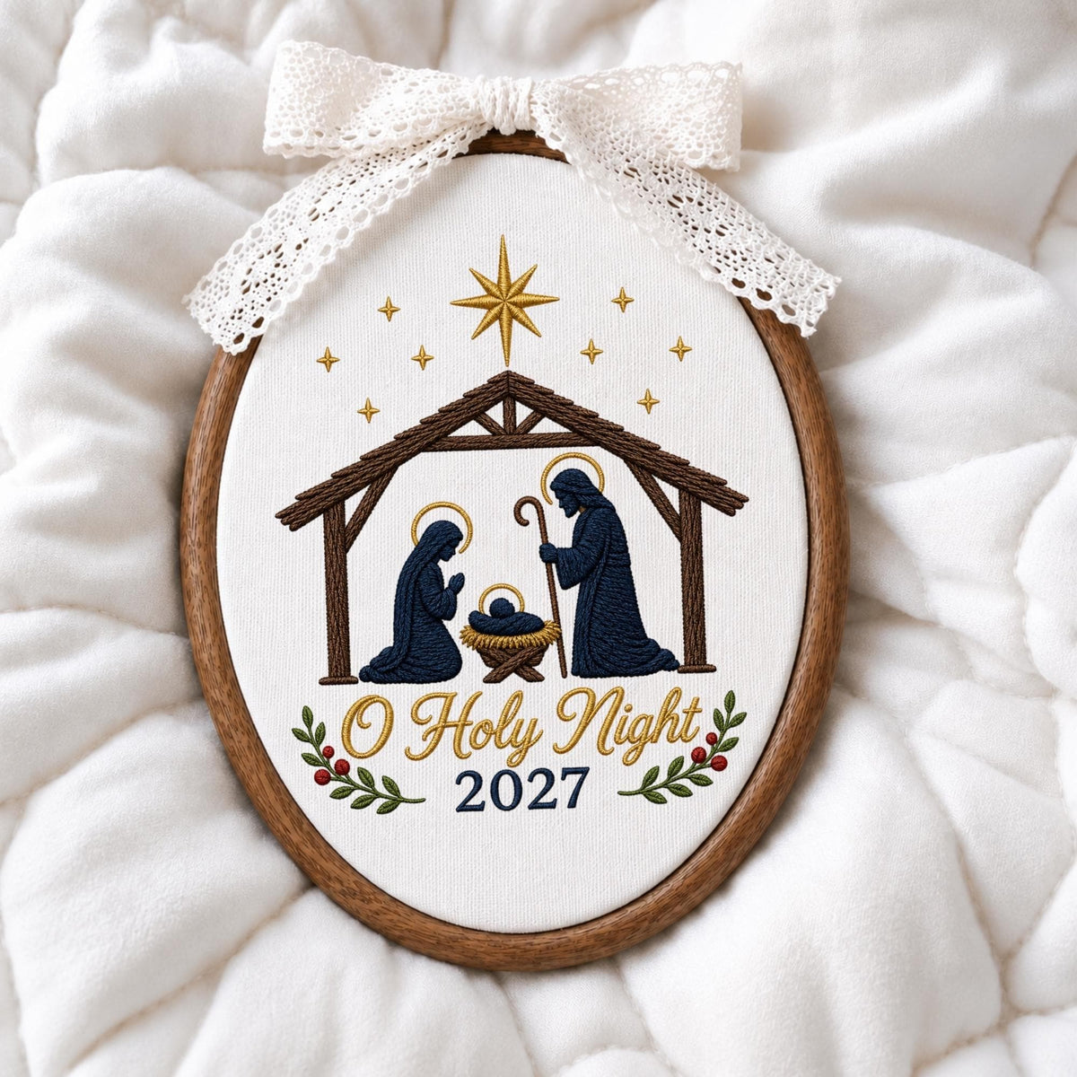 May include: An oval embroidery hoop featuring a nativity scene with dark blue figures of Mary, Joseph, and baby Jesus under a brown wooden stable. Above is a gold star and smaller stars. The text O Holy Night 2027 is embroidered with a lace bow.