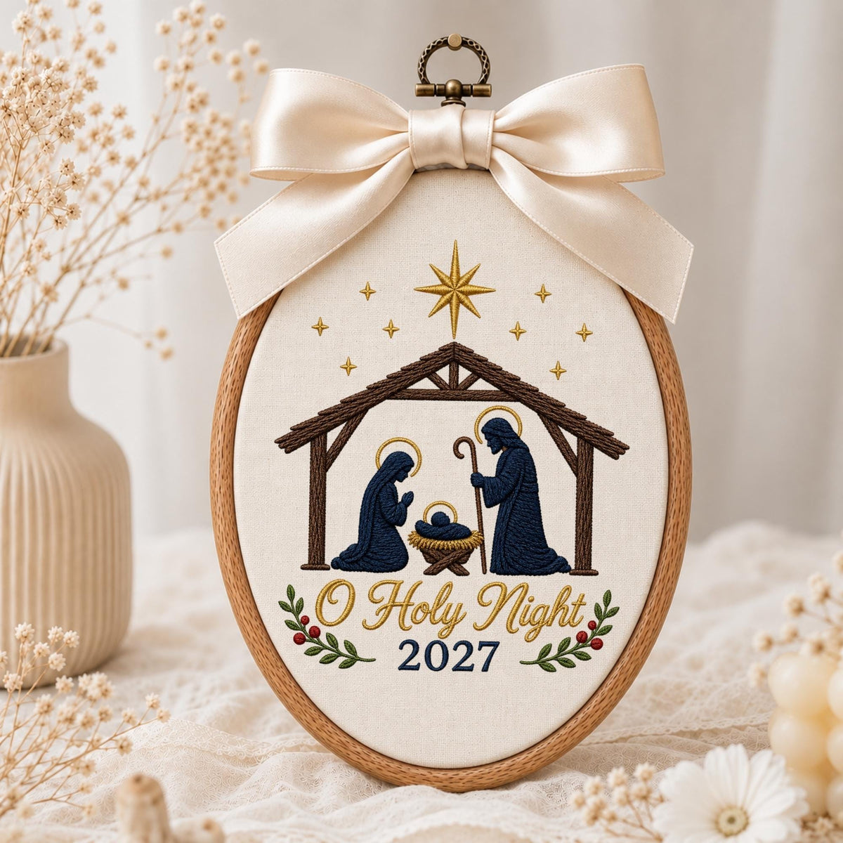 May include: An oval embroidery hoop featuring a nativity scene with Mary, Joseph, and baby Jesus in a manger under a star. The fabric is cream-colored with the text O Holy Night 2027 embroidered in gold and blue, topped with a large cream satin bow.
