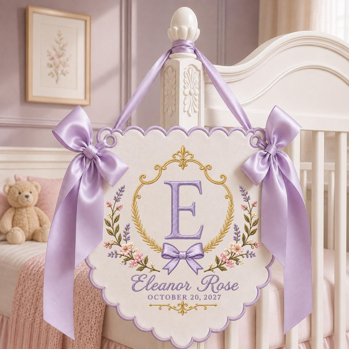 May include: A white scalloped wall hanging featuring an embroidered gold frame, a large purple letter E, and the text Eleanor Rose October 20, 2027. The sign is decorated with floral embroidery and two large lavender satin bows on the top corners.