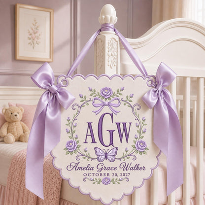 May include: A cream-colored scalloped wall hanging featuring purple embroidered roses, a butterfly, and the monogram AGW. The text reads Amelia Grace Walker and OCTOBER 20, 2027. It is adorned with two large lavender satin bows and matching ribbon ties.