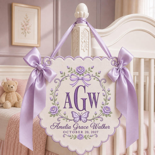 May include: A cream-colored scalloped wall hanging featuring purple embroidered roses, a butterfly, and the monogram AGW. The text reads Amelia Grace Walker and OCTOBER 20, 2027. It is adorned with two large lavender satin bows and matching ribbon ties.