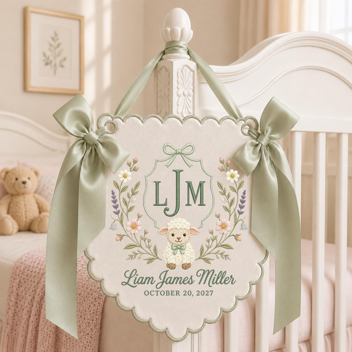 May include: A cream-colored scalloped wall hanging featuring an embroidered lamb, floral wreath, and the monogram LJM. The text reads Liam James Miller and October 20, 2027. It is accented with sage green satin ribbons tied at the top corners.