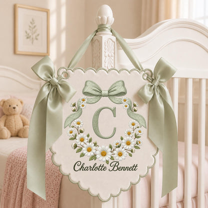 May include: A cream-colored fabric wall hanging with a scalloped edge, featuring an embroidered sage green letter C surrounded by a wreath of white daisies. The banner is accented with two sage green satin bows and the name Charlotte Bennett.