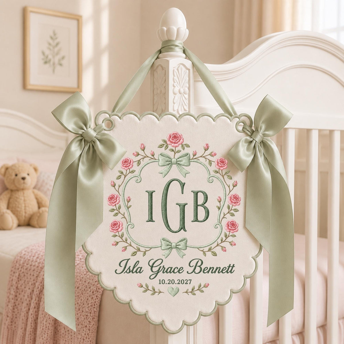 May include: A cream-colored scalloped fabric wall hanging featuring an embroidered floral wreath with pink roses and sage green bows. The center displays the monogram IGB in dark green, with the name Isla Grace Bennett and date 10.20.2027 below.