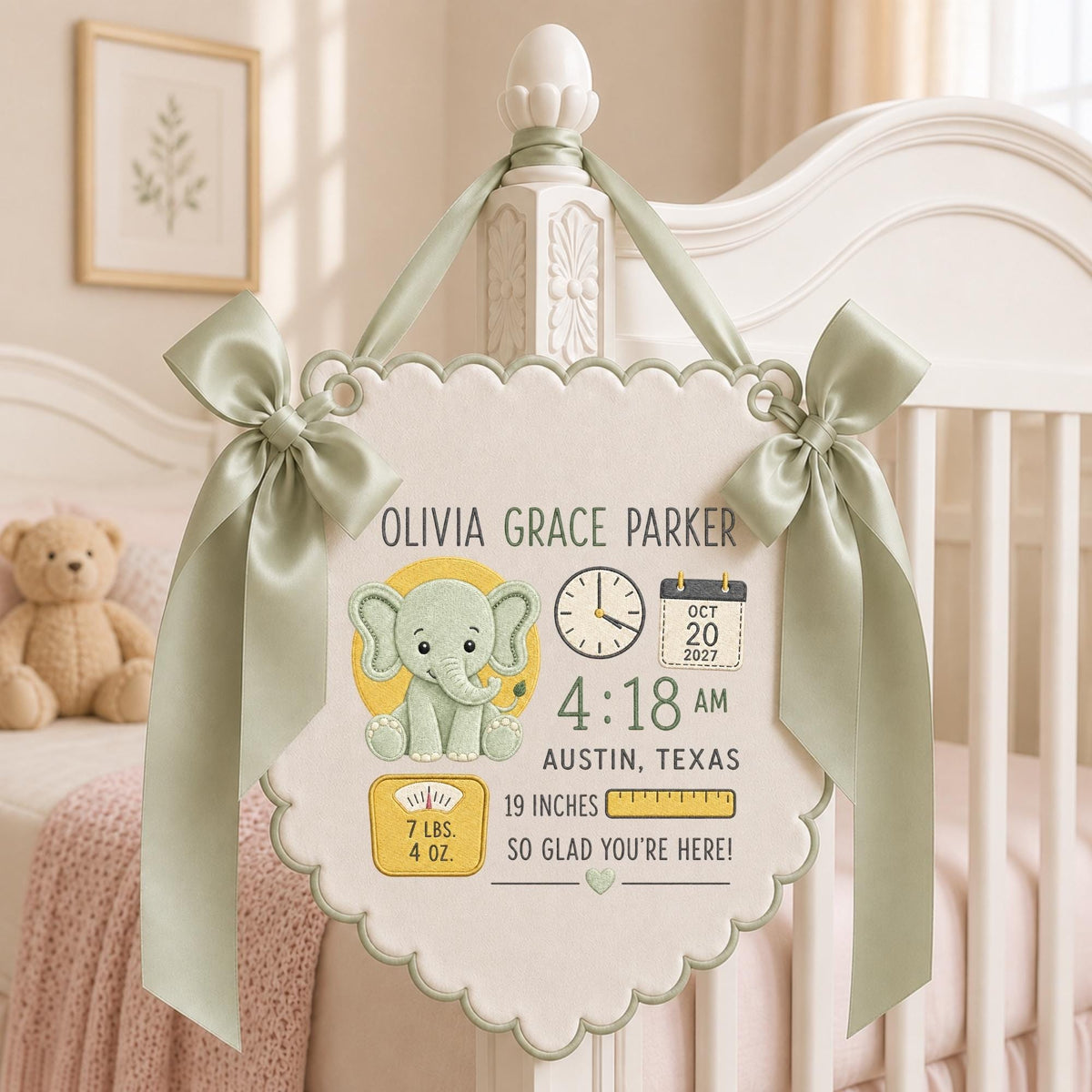 May include: A cream-colored fabric wall hanging with scalloped edges and sage green ribbon bows. It features an embroidered elephant, a clock, a calendar showing Oct 20 2027, the name Olivia Grace Parker, 4:18 AM, Austin, Texas, 19 inches, 7 lbs. 4 oz.