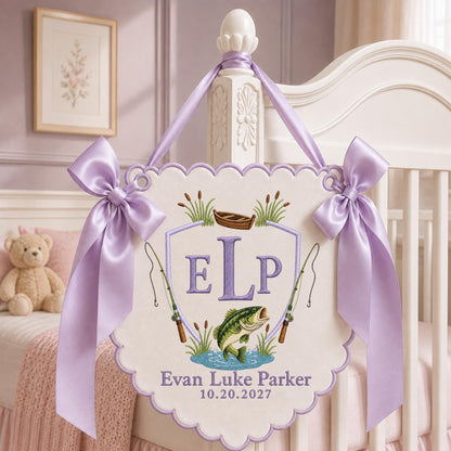 May include: A cream-colored scalloped wall hanging featuring an embroidered shield with the letters ELP, a small boat, two fishing rods, and a green fish. The name Evan Luke Parker and the date 10.20.2027 are stitched below, accented by lavender satin bows.