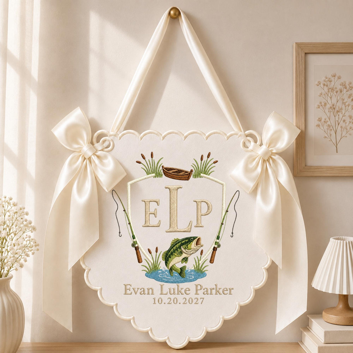 May include: A cream-colored scalloped wall hanging featuring an embroidered design with the monogram ELP, a brown boat, two fishing rods, and a green fish. The text reads Evan Luke Parker and 10.20.2027. It is accented with two large satin bows.