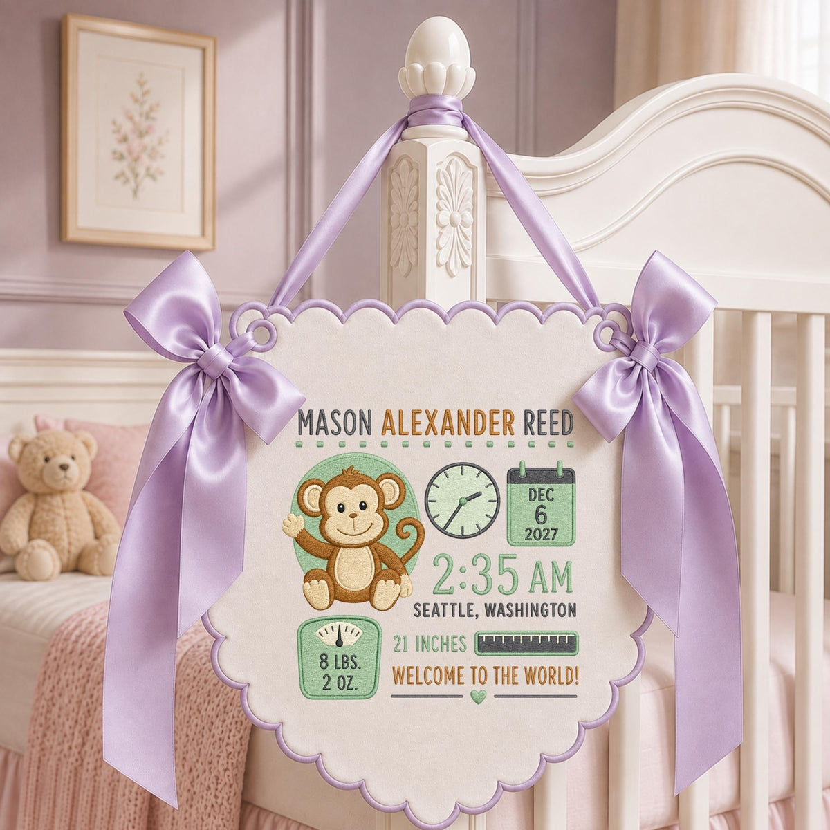 May include: A cream-colored fabric wall hanging with scalloped edges and lavender satin bows. It features embroidered details: a brown monkey, a clock, a calendar showing Dec 6 2027, a scale reading 8 lbs. 2 oz., a ruler, and text: MASON ALEXANDER REED, 2:35 AM, SEATTLE, WASHINGTON, 21 INCHES, WELCOME TO THE WORLD!