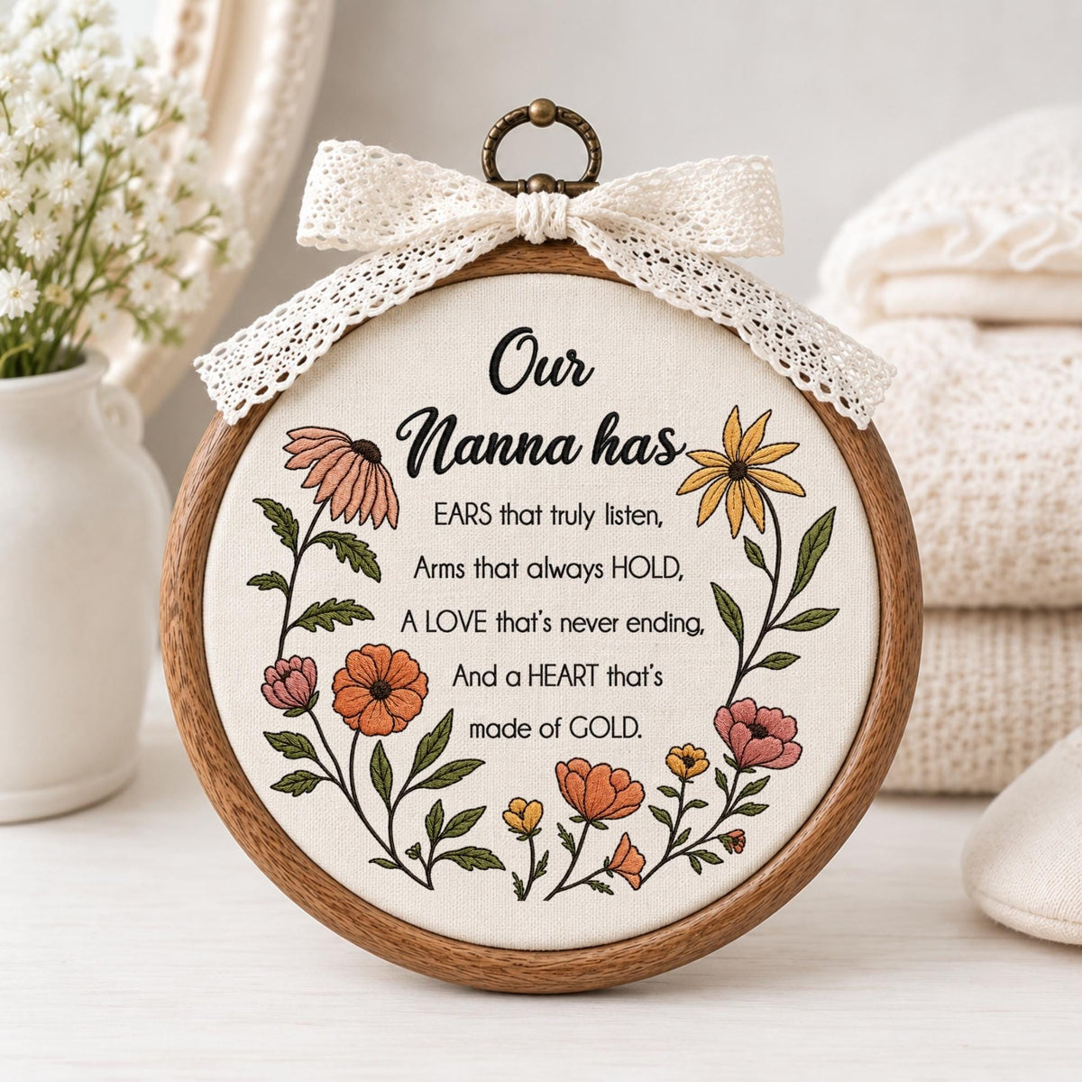 May include: A circular wooden embroidery hoop containing off-white fabric with floral embroidery and black text reading: Our Nanna has EARS that truly listen, Arms that always HOLD, A LOVE that's never ending, And a HEART that's made of GOLD. A lace bow sits on top.