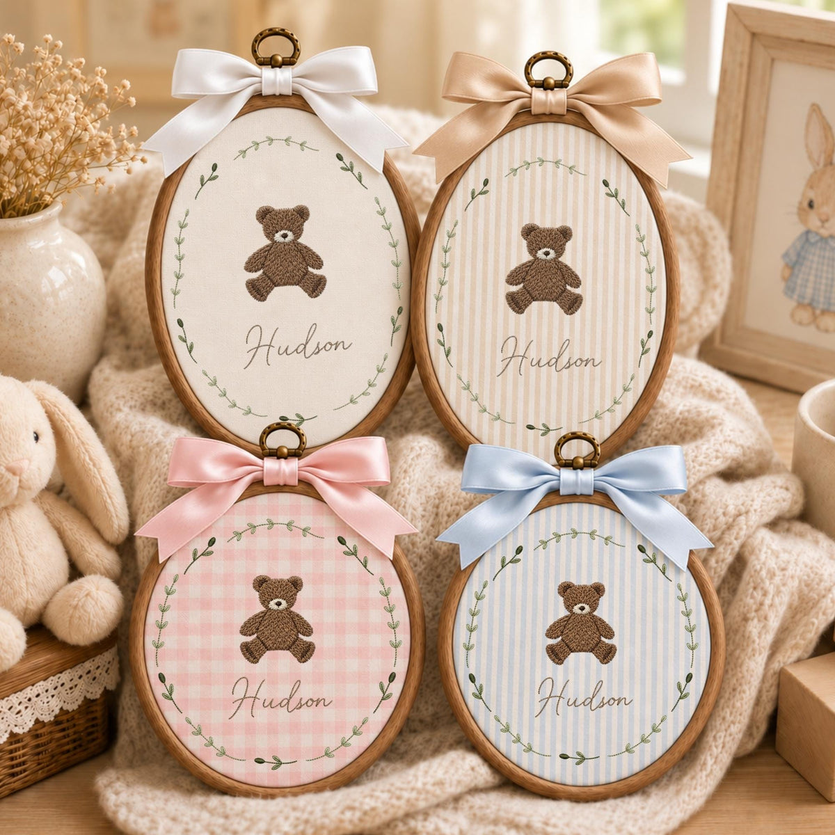 May include: Four oval wooden embroidery hoops featuring fabric centers with embroidered brown teddy bears and the name Hudson in cursive script. Each hoop is decorated with a satin ribbon bow at the top and a green leaf wreath border.