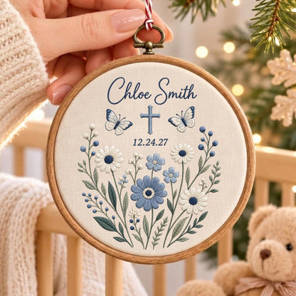 May include: A circular wooden embroidery hoop containing off-white fabric with blue floral embroidery, two butterflies, a cross, and the text Chloe Smith 12.24.27. The design features various blue and white flowers with green stems and leaves.
