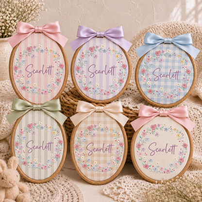 May include: Six oval wooden embroidery hoops featuring fabric backgrounds with stripes or gingham patterns. Each hoop displays a floral wreath surrounding the name Scarlett in purple script and is topped with a satin ribbon bow in various colors.