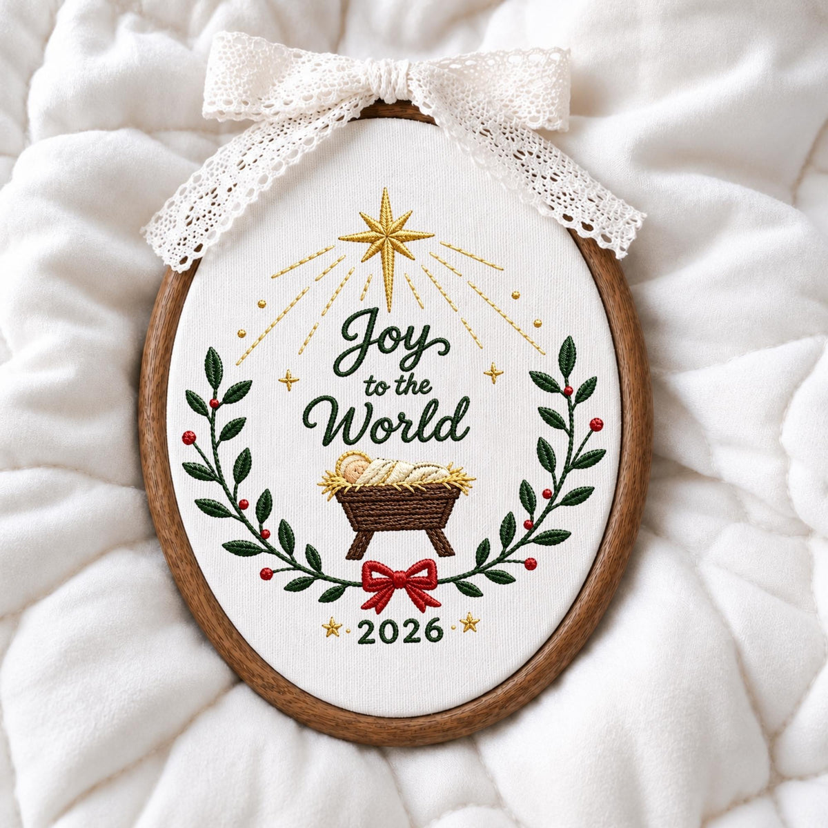 May include: An oval embroidery hoop containing white fabric with the embroidered text Joy to the World and 2026. The design features a gold star, a manger with a baby, green holly leaves with red berries, and a red bow. A white lace bow is attached.