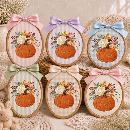 May include: Six oval embroidery hoops featuring fabric backgrounds with stripes or gingham patterns. Each hoop displays an embroidered orange pumpkin with the word thankful, topped with a floral arrangement and a satin ribbon bow.
